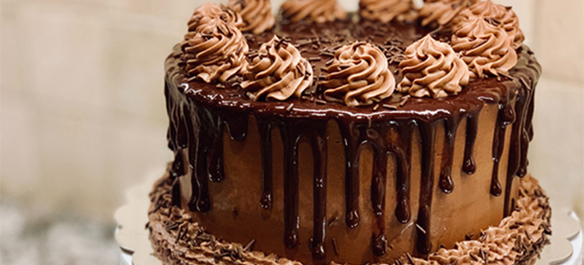 This cake is perfect for any chocolate lover. It features a Red Velvet cake and a rich chocolate frosting. It is coated with chocolate ganache drips, chocolate buttercream swirls, and garnished with chocolate shavings.