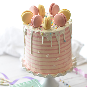 This cake features strawberry buttercream frosting that is placed between 4 lemon rounds. It is topped with french macaroons.